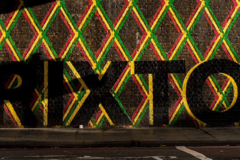 Artist painted Brixton in black and a mixed colour border on a wall under Brixton Rail bridge