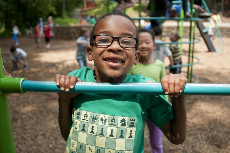 Smiling boy with glasses hanging off frame in playground