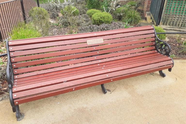 photo of an S8 victorian style memorial bench with brick red slats and black arms