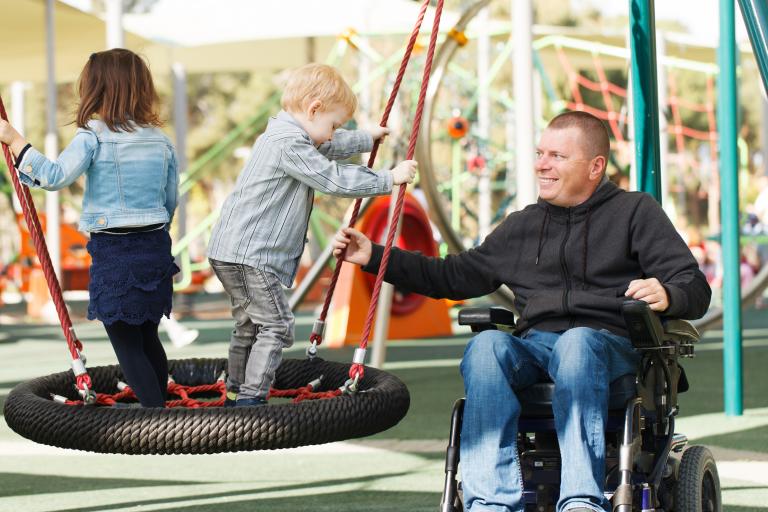 Man in wheelchair helping children in playground