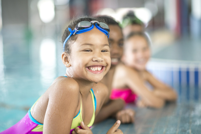 Smiling children leaning on the edge of a swimming pool with googles on their head