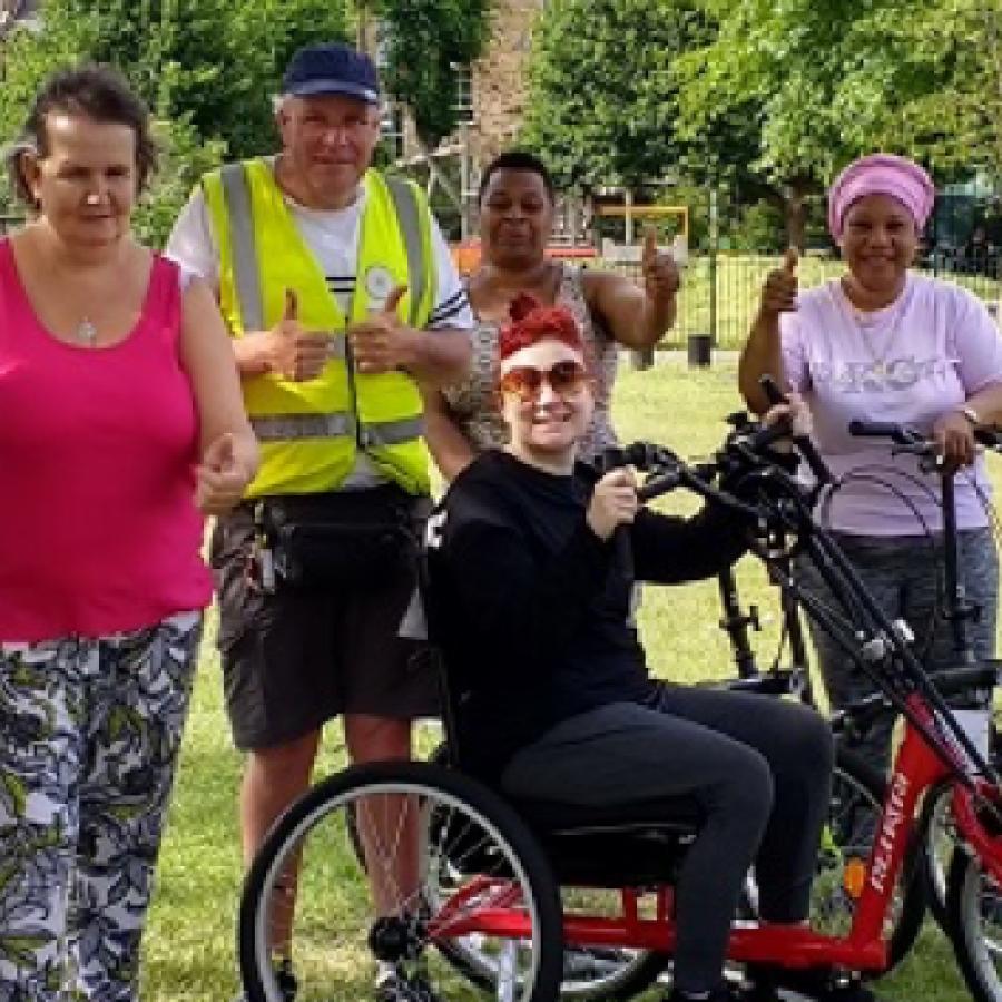 A range of different people posing for a photo in a park holding their thumbs up