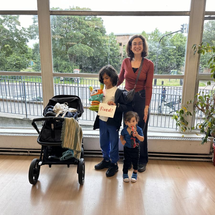 Mother & child standing with toy and 'fixed' label from the Repairs Cafe at we are 336